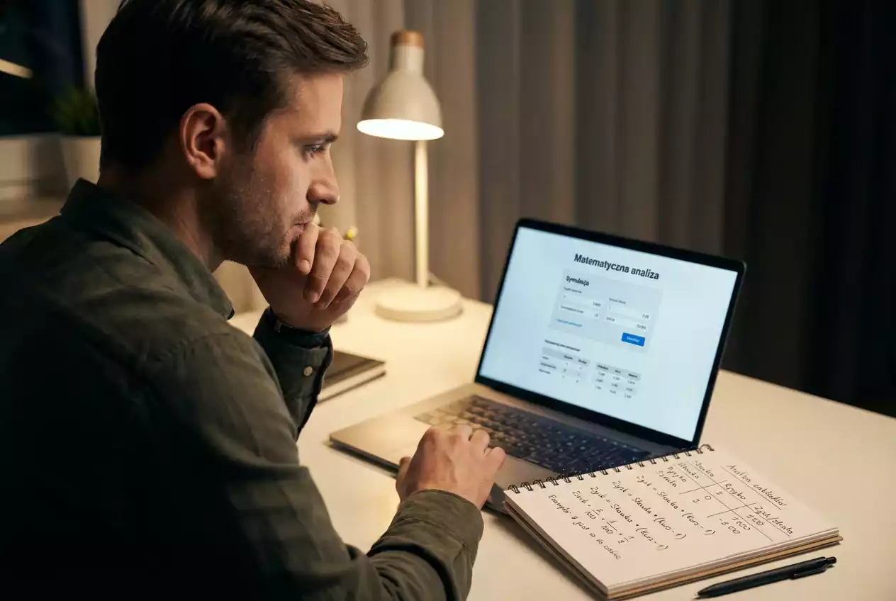 Osoba analizująca dane liczbowe na laptopie z notatkami obok